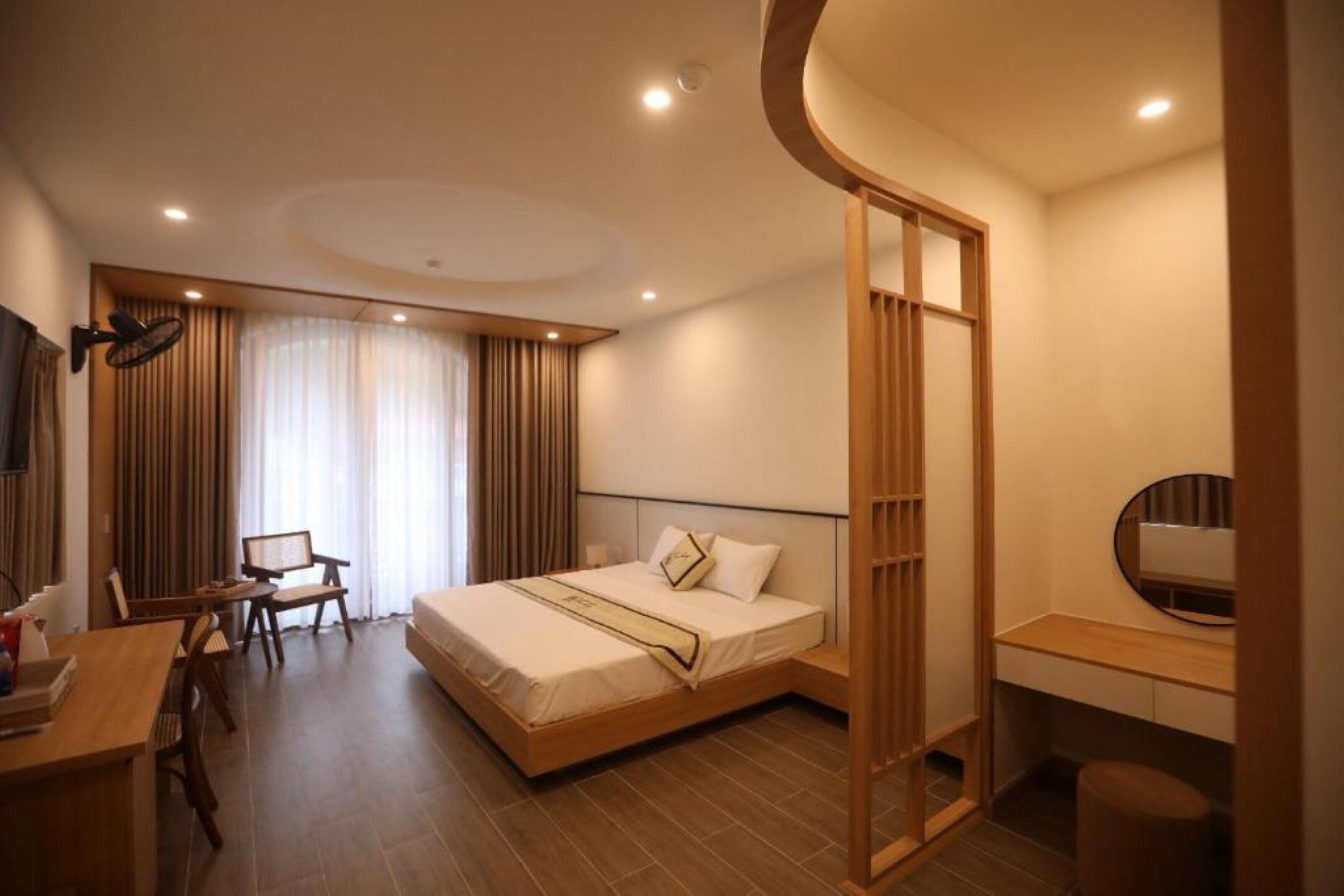 A hotel room with a bed, desk, chair, and a large window with curtains.