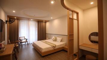 A hotel room with a bed, desk, chair, and a large window with curtains.