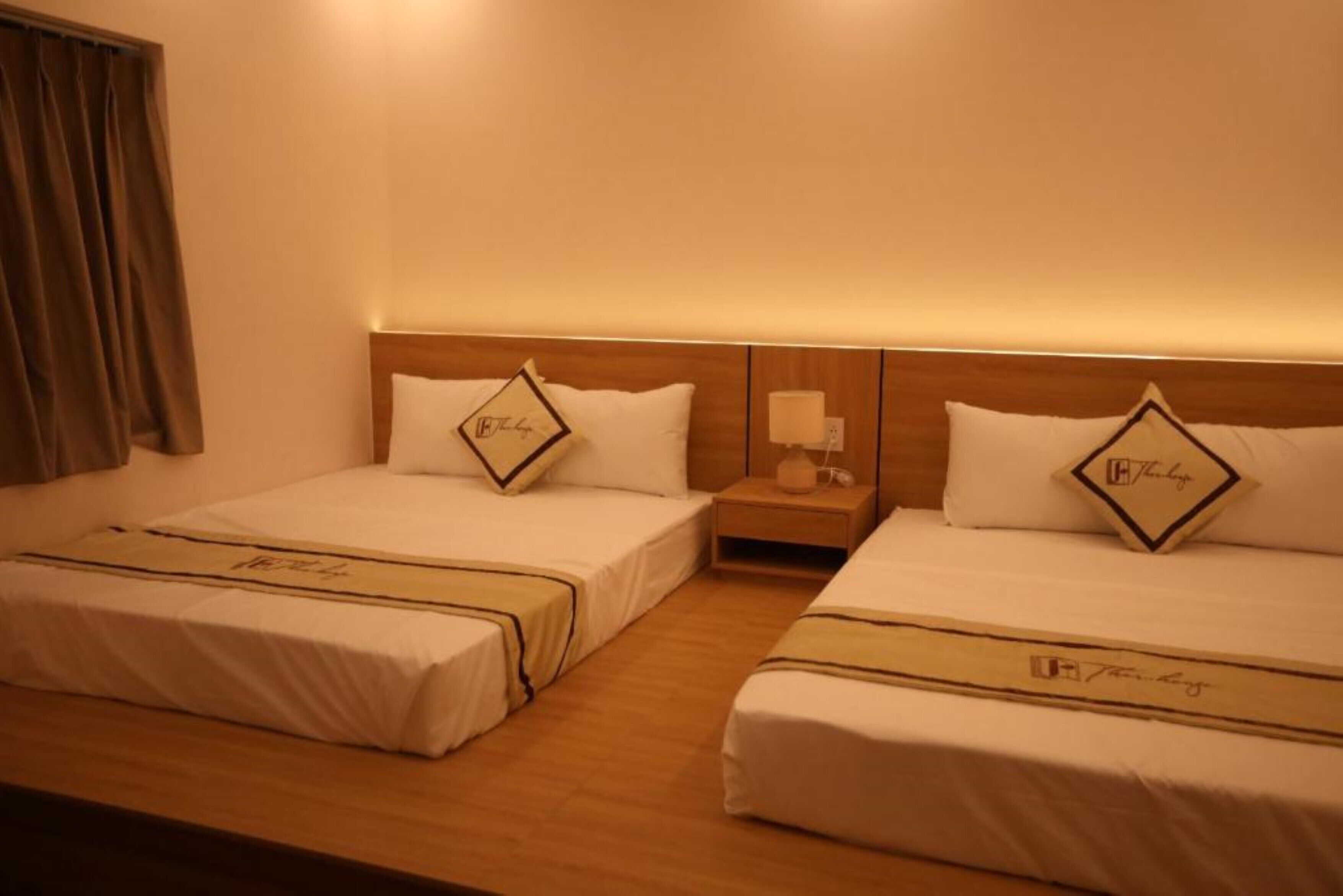 A hotel room with two beds, each with a matching pillow and a bedside table with a lamp.
