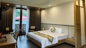 Ein Hotelzimmer mit einem Bett, einem Schreibtisch und einem Stuhl. Ein Fenster mit Vorhängen bietet Blick auf ein Gebäude.