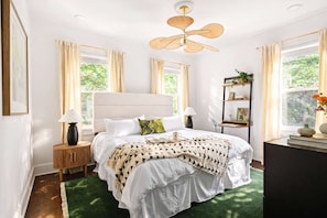 A bedroom with a bed, bedside tables, a ceiling fan, a bookshelf, and a window with curtains.