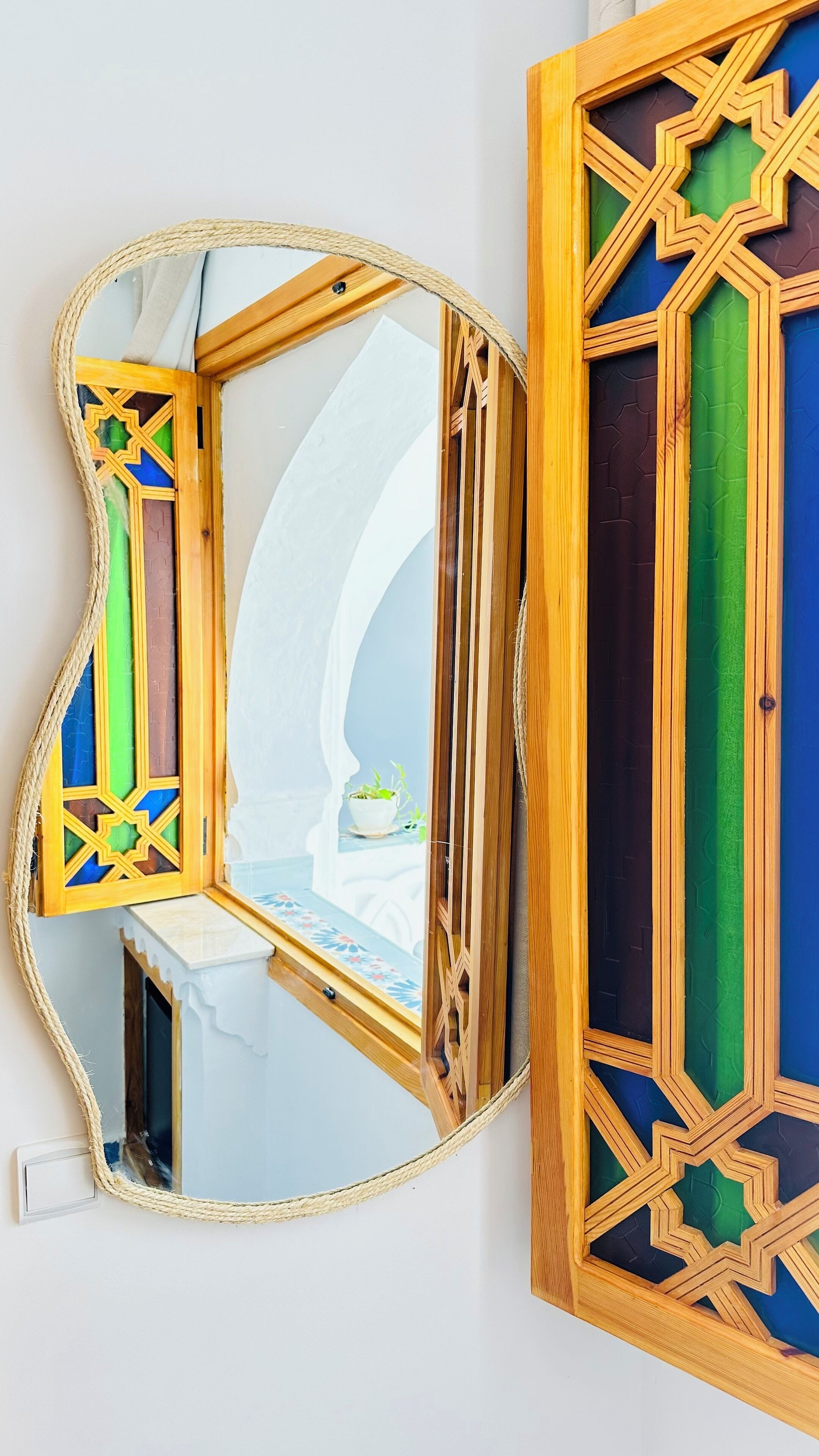 Una habitación con un espejo grande que refleja una esquina, una pequeña mesa con una planta y una pared blanca.