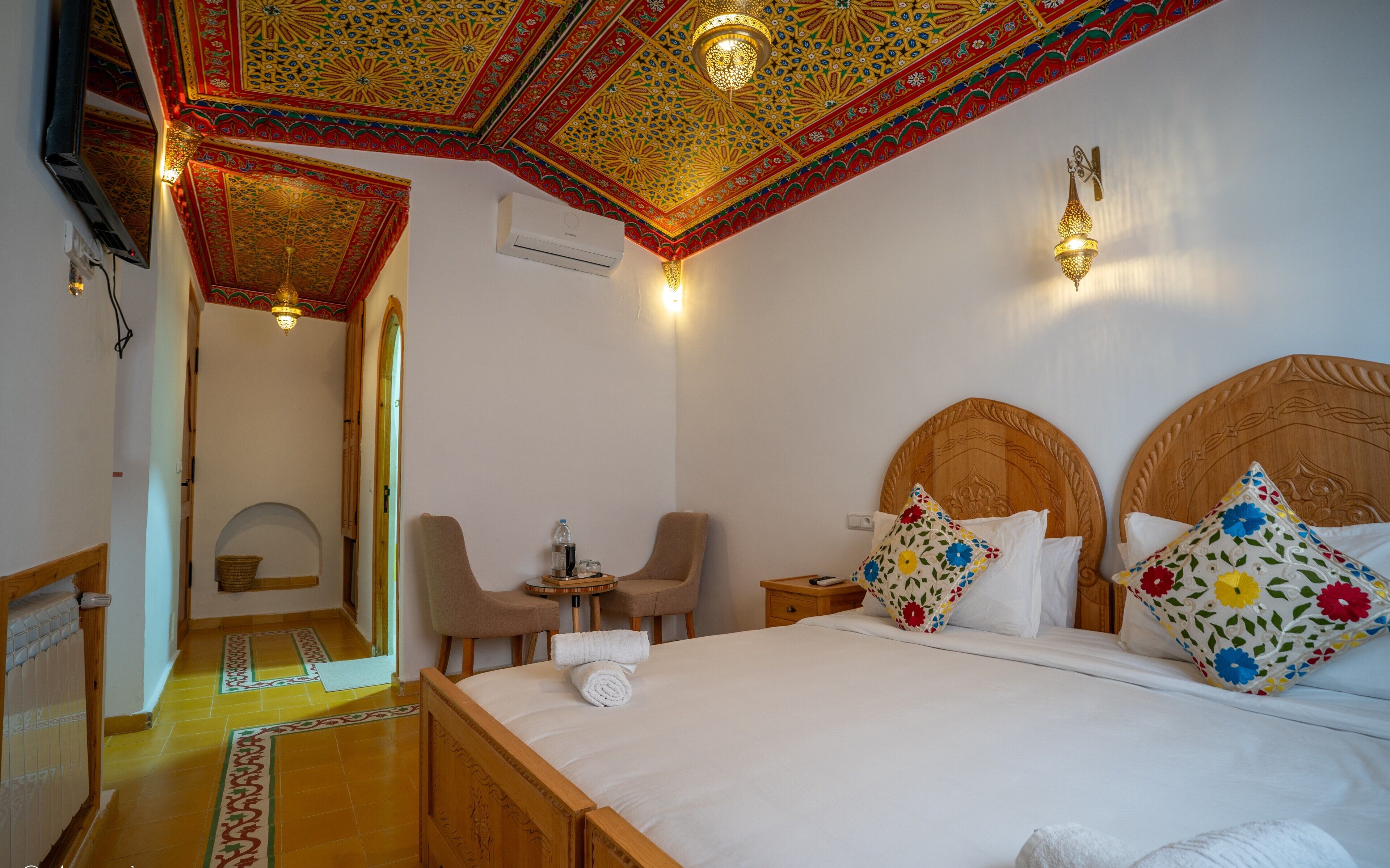 Une chambre d’hôtel avec un grand lit, un bureau, une chaise et une salle de bain visible à travers une arche.