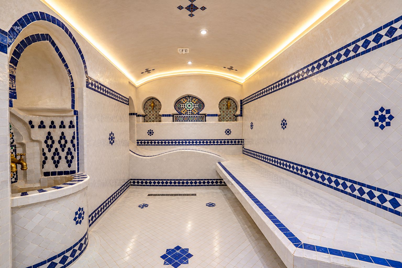 Une salle de bain aux murs recouverts de carreaux blancs et bleus, avec un lavabo et un espace douche.