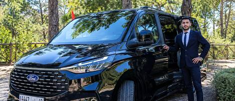En sort Ford SUV holder parkeret udenfor, med en mand i jakkesæt stående ved siden af den.