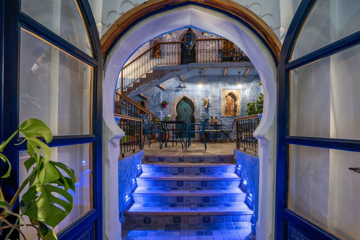 A staircase leading to a room with a view of a building, a dining area with chairs and tables, and a potted plant.