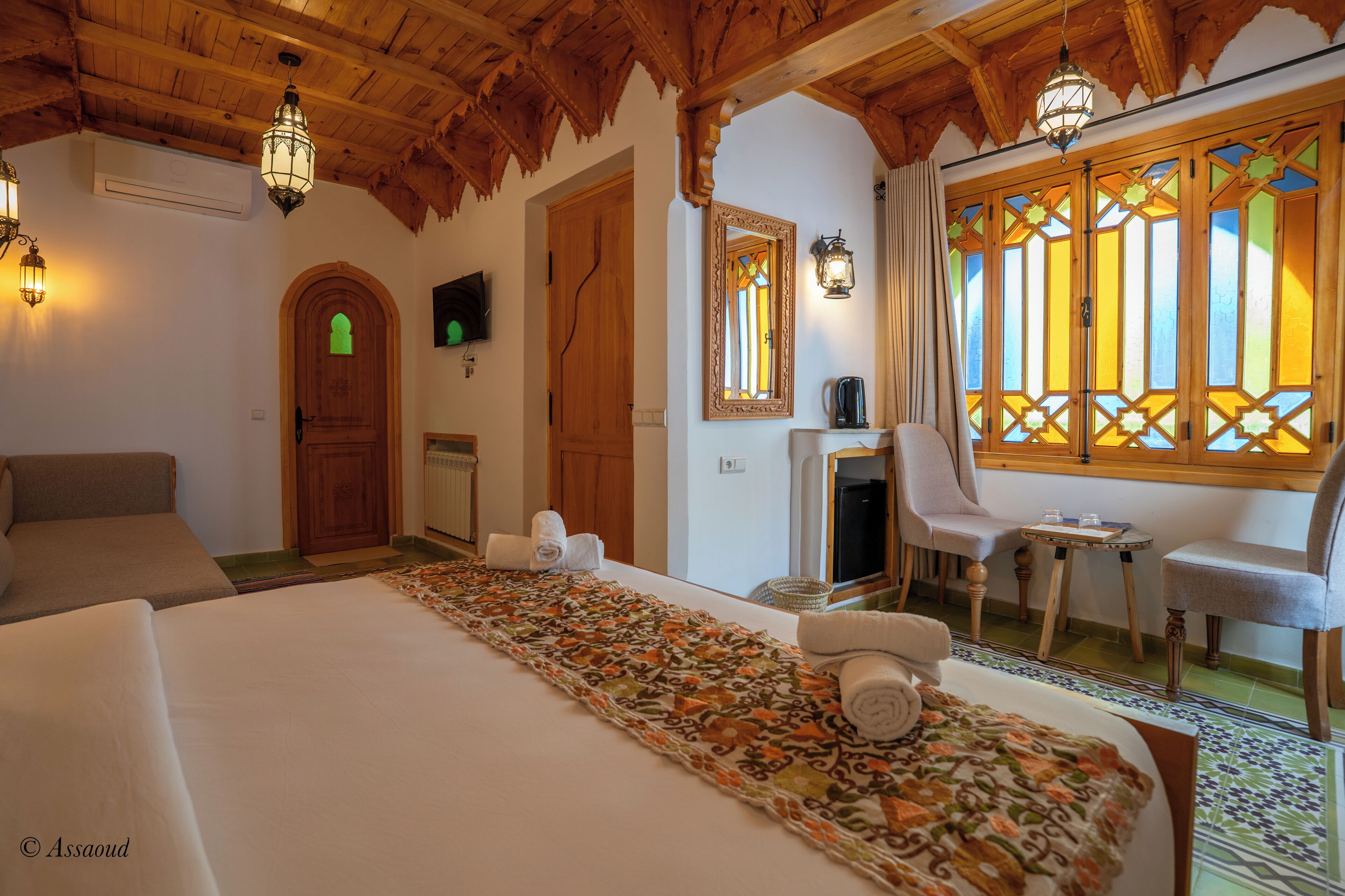 Habitación de hotel con una cama grande, techo de madera, televisor y una ventana con vidrieras.