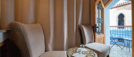 Una habitación con dos sillones color beige, una mesa de vidrio con servilletas y vista a un patio azul con piso de baldosas.