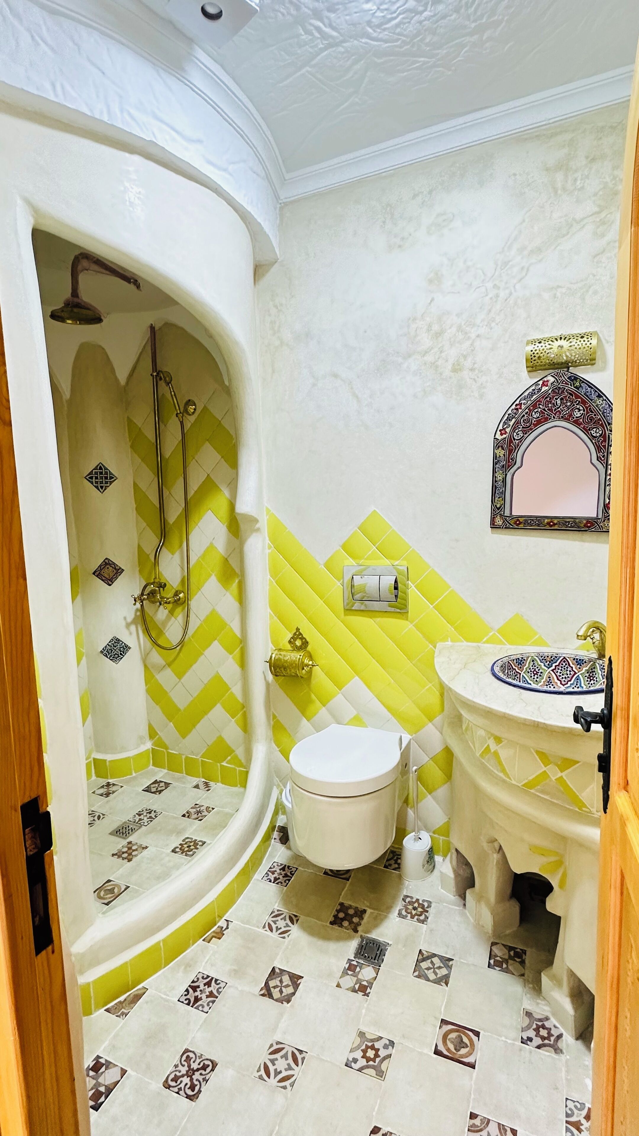 Un baño con ducha, inodoro y lavamanos, con baldosas estampadas y un espejo decorativo.