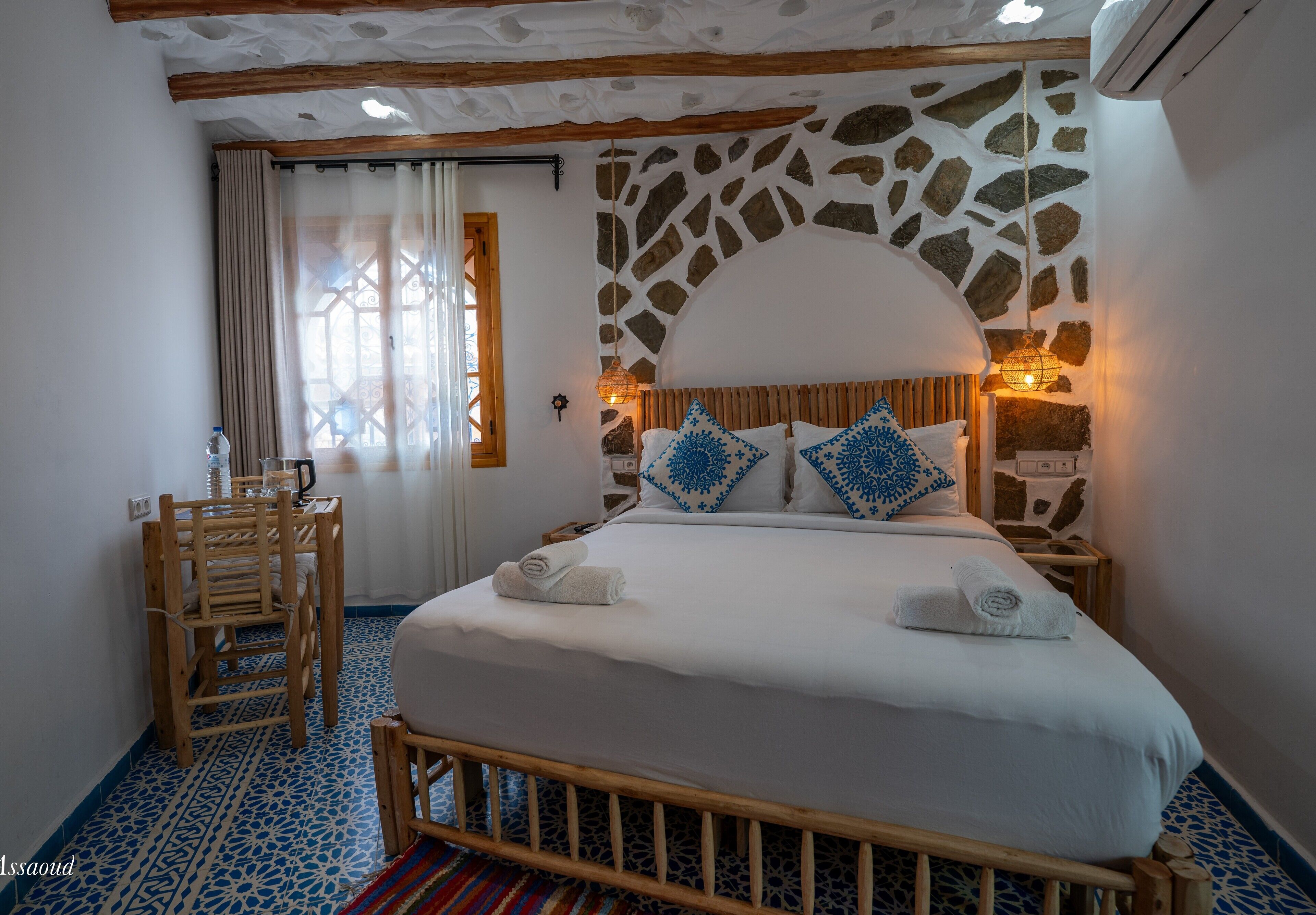 Un dormitorio con pared de piedra, estructura de cama de madera y suelo estampado.