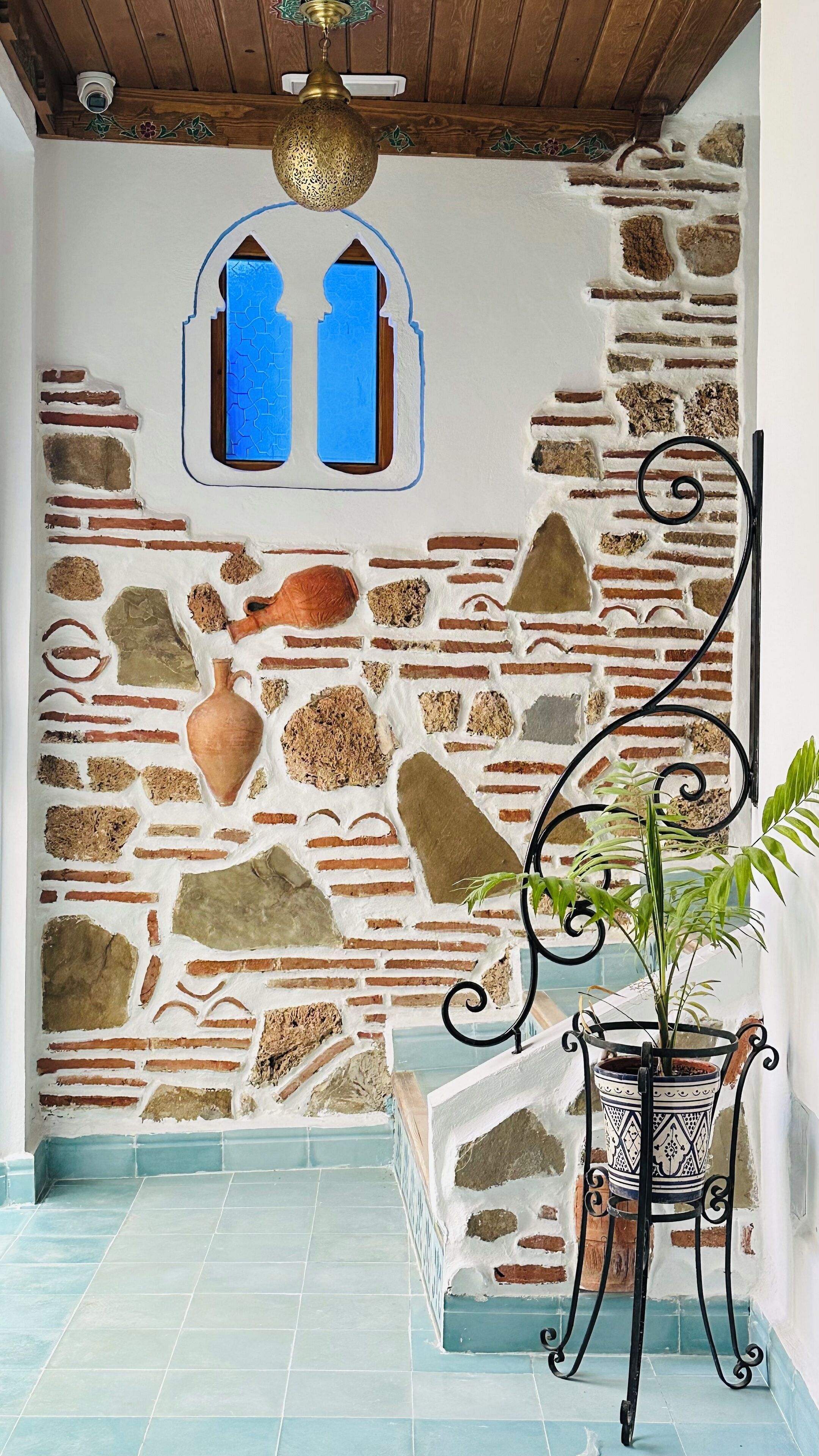 A room with a stone wall, a blue-tiled floor, a potted plant, and a decorative metal chair.