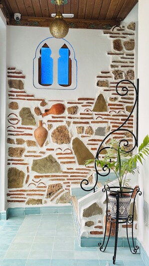 Een kamer met een stenen muur, een vloer van blauwe tegels, een potplant en een decoratieve metalen stoel.