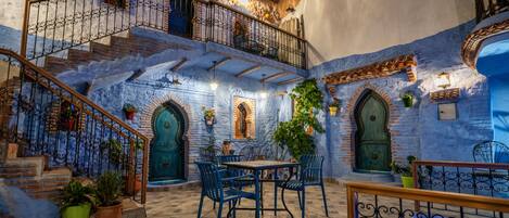 A courtyard with a staircase, a table with chairs, and potted plants.