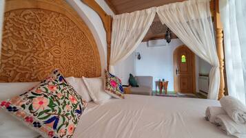 Un dormitorio con una cama grande, un cabecero ornamentado, almohadas estampadas con motivos florales y dosel.