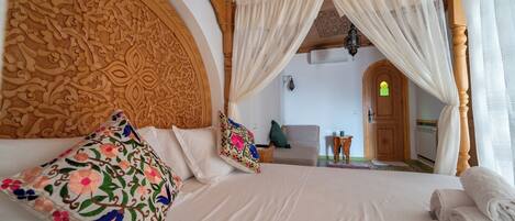 A bedroom with a large bed, ornate headboard, floral pillows, and a canopy bed.
