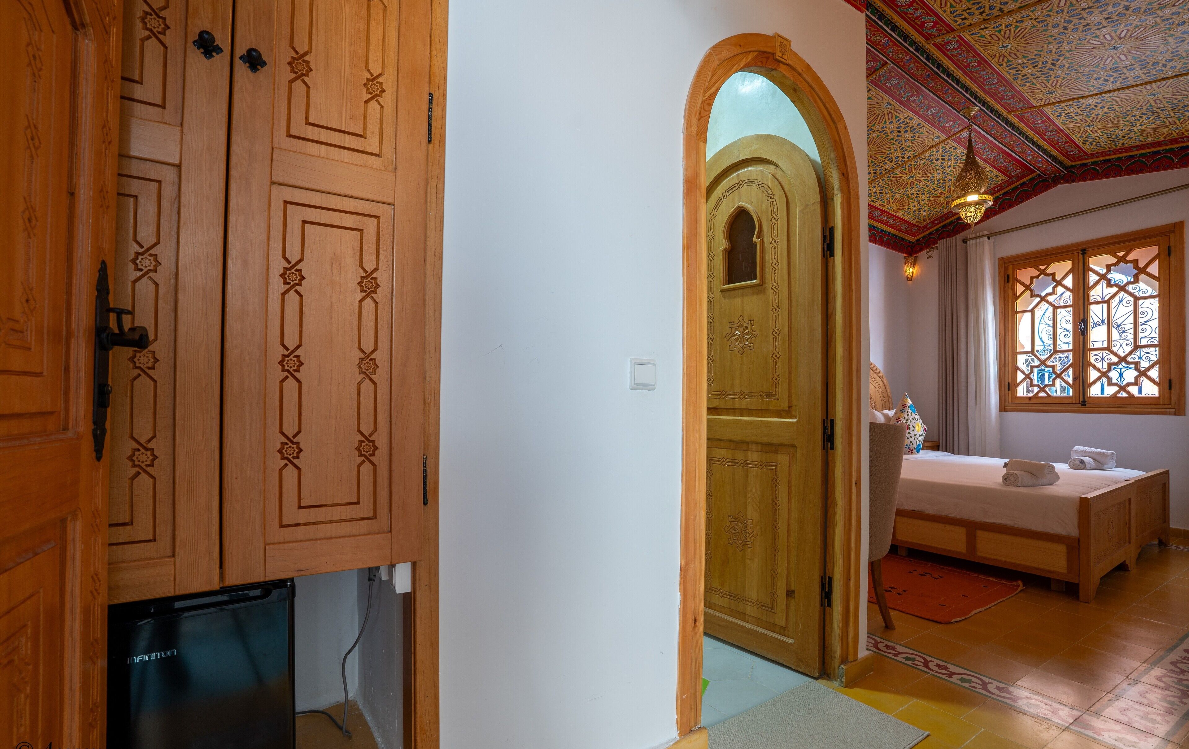 Een hotelkamer met een houten deur, een bed, een raam met ingewikkelde patronen en een plafond met gedetailleerde decoraties.