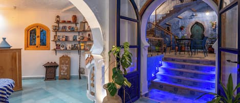 Un vestíbulo espacioso con una escalera que lleva a un balcón, un jarrón grande con una planta y una estantería llena de libros y objetos decorativos.
