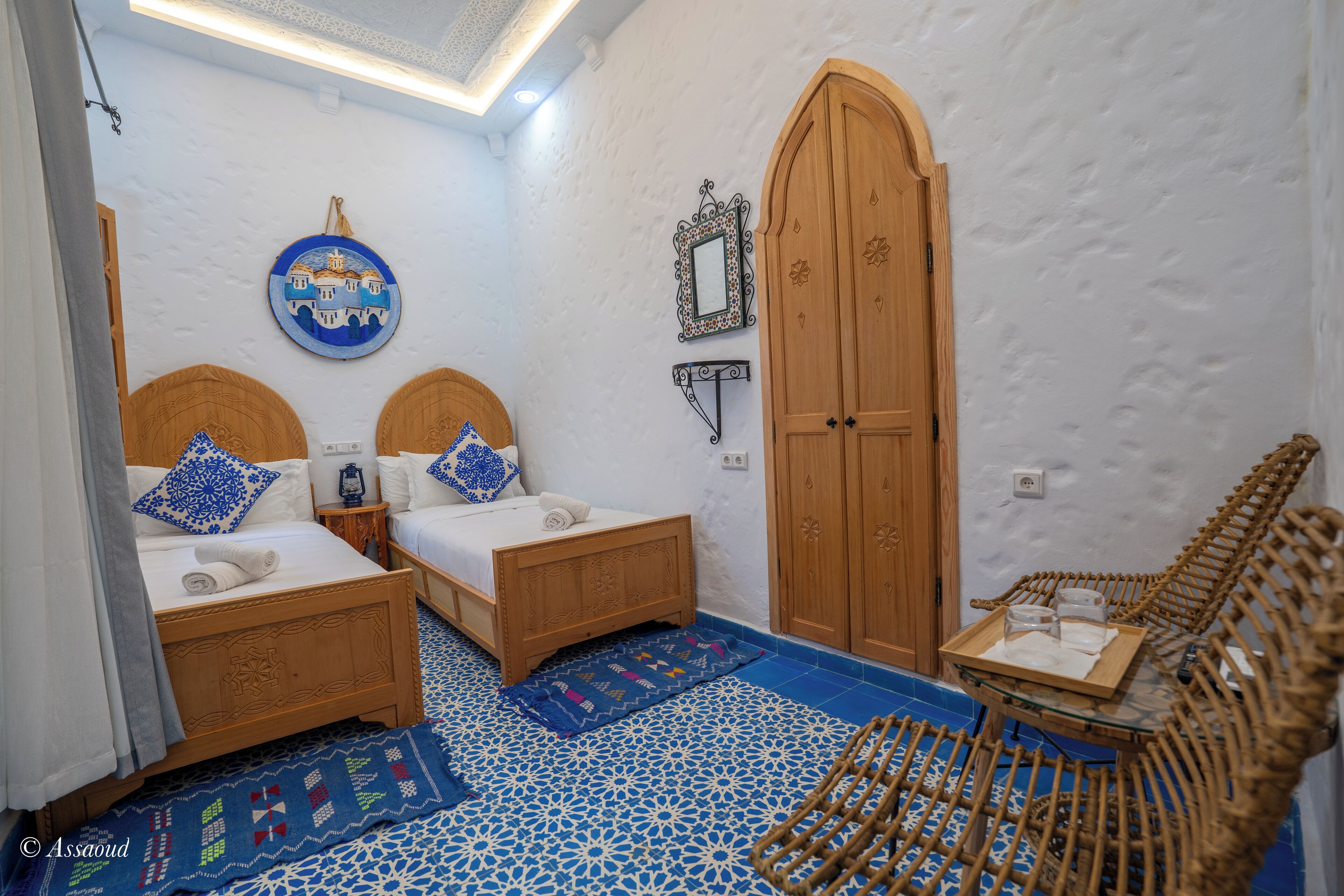 A room with two wooden beds, a large wooden door, a rattan chair, and a blue patterned floor.