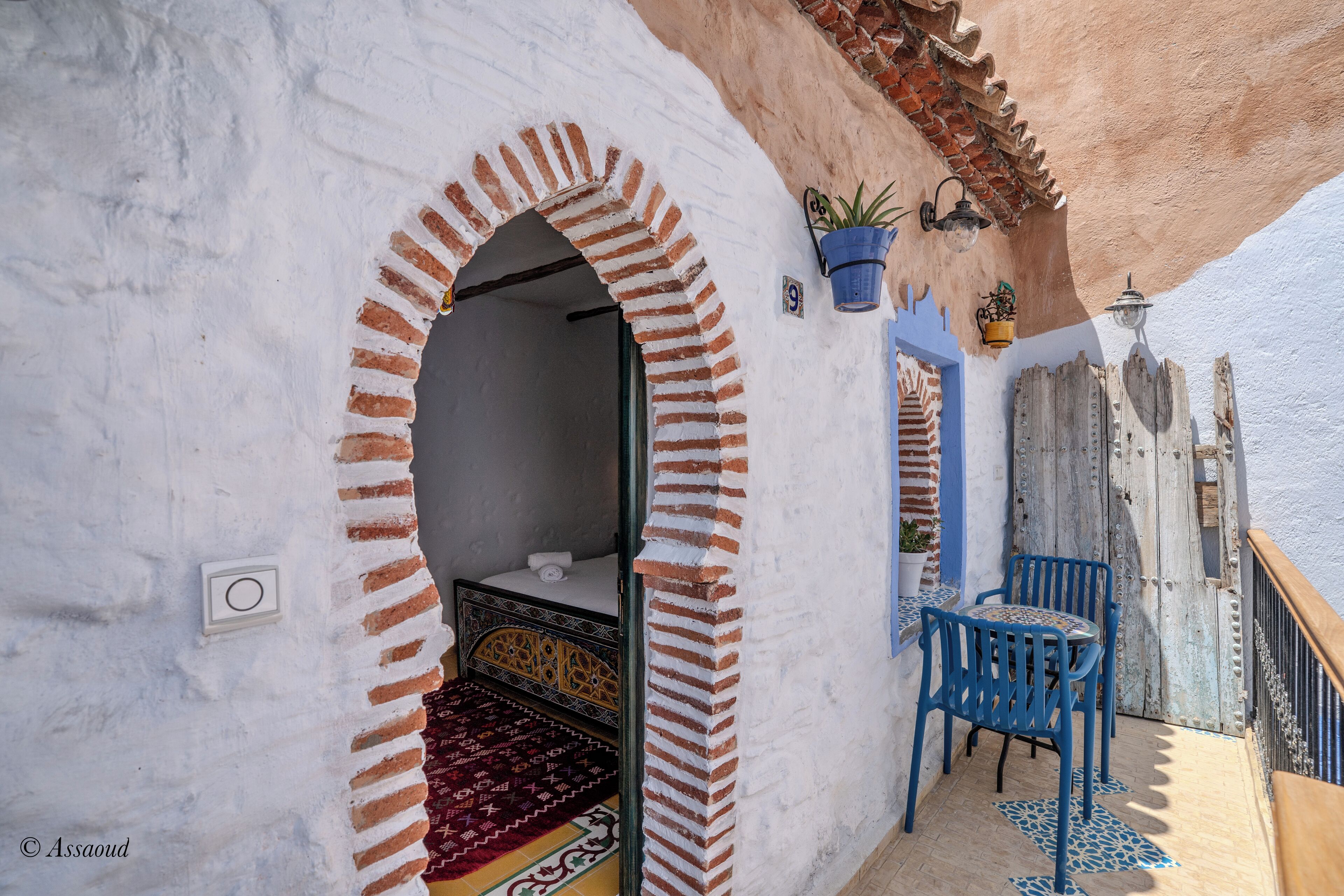 A room with a traditional design, featuring a patterned rug, a bed with a headboard, and a small table with chairs.