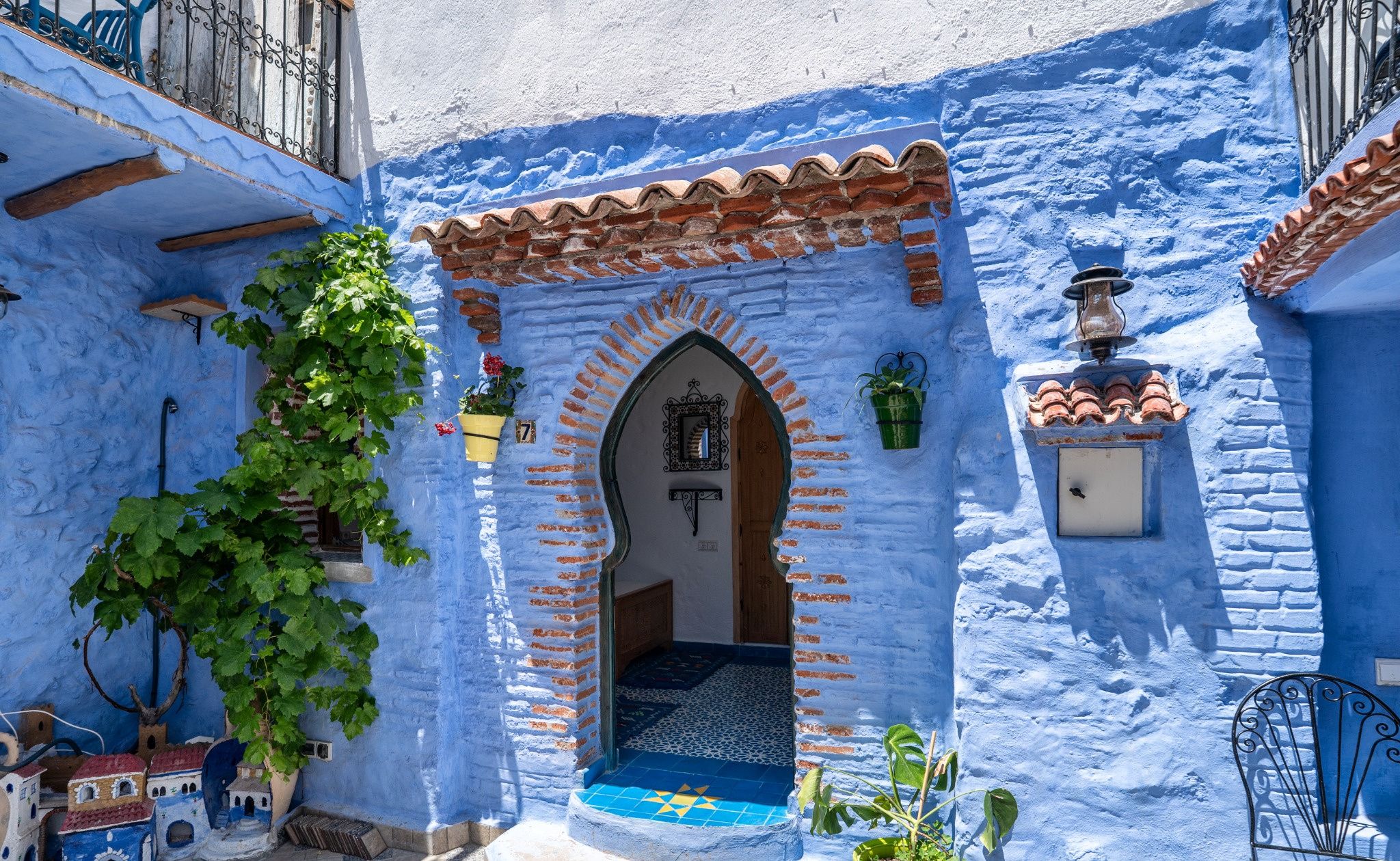 A traditional blue-walled building with a tiled entrance, a hanging plant, and a small balcony.