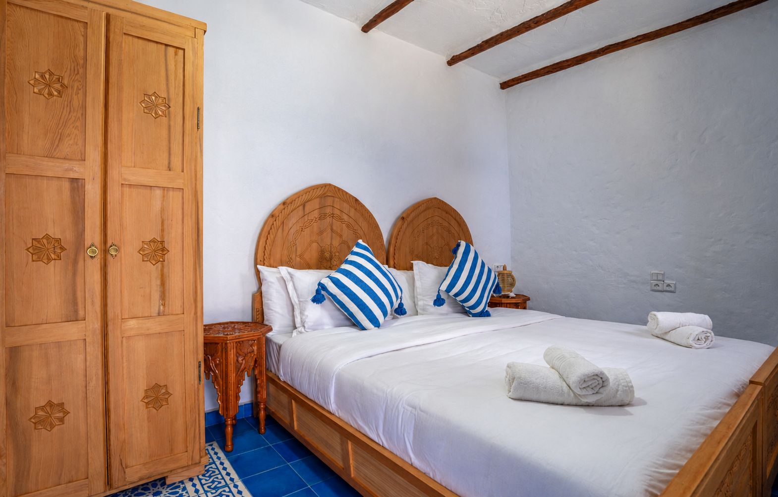 A bedroom with a wooden wardrobe, a bed with white bedding, and a blue and white striped pillow.