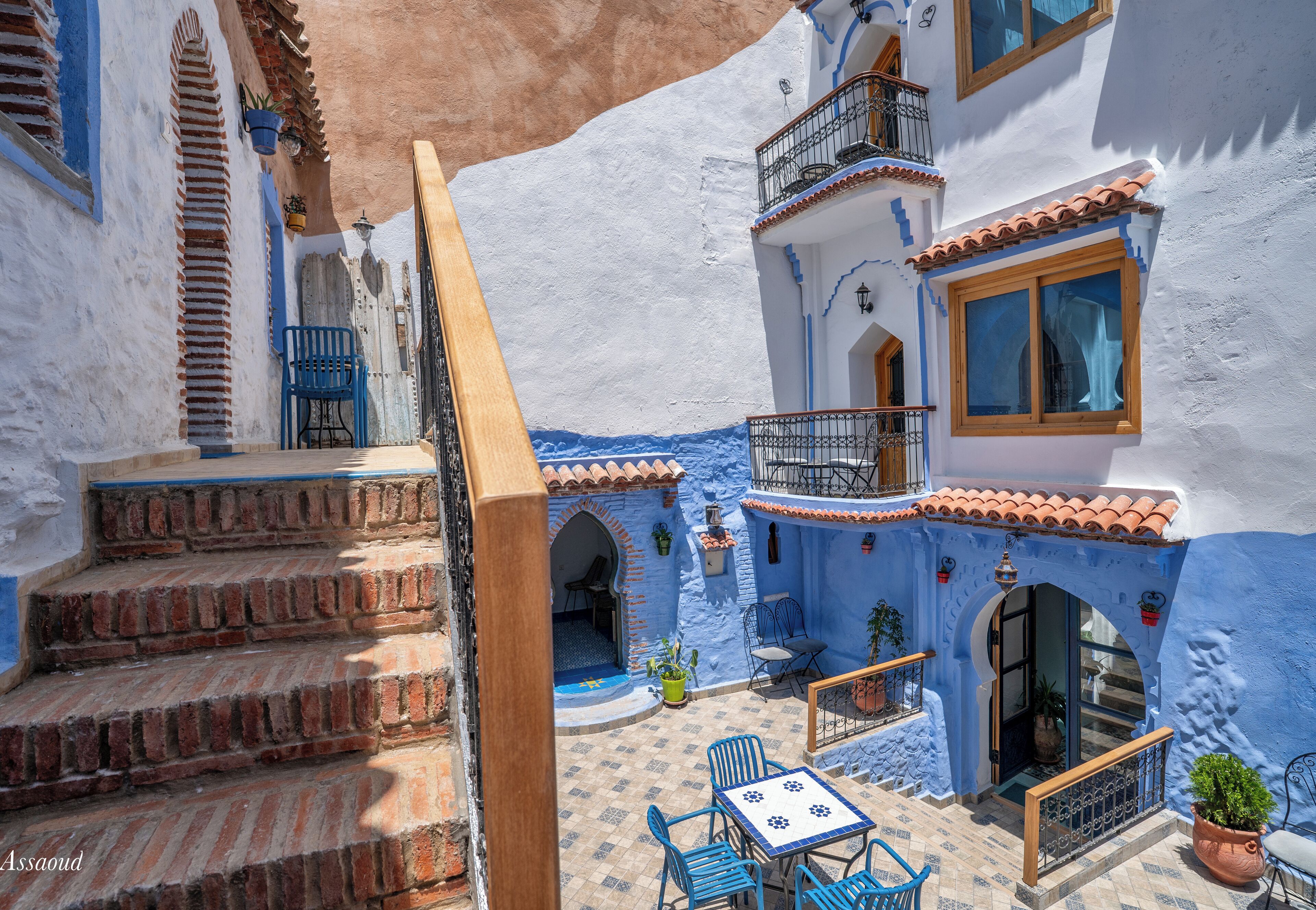 A courtyard with a table and chairs, a staircase, and a balcony with a railing.