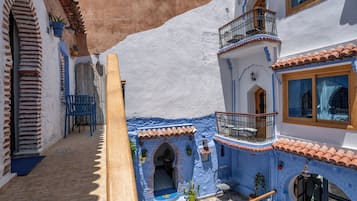 A courtyard with a blue and white building, a wooden bench, and potted plants.