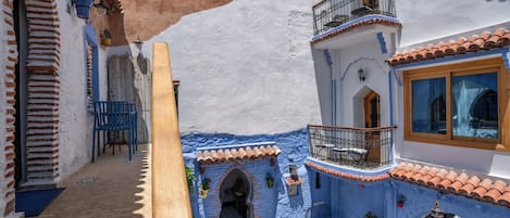 Un patio con un edificio azul y blanco, un banco de madera y plantas en macetas.