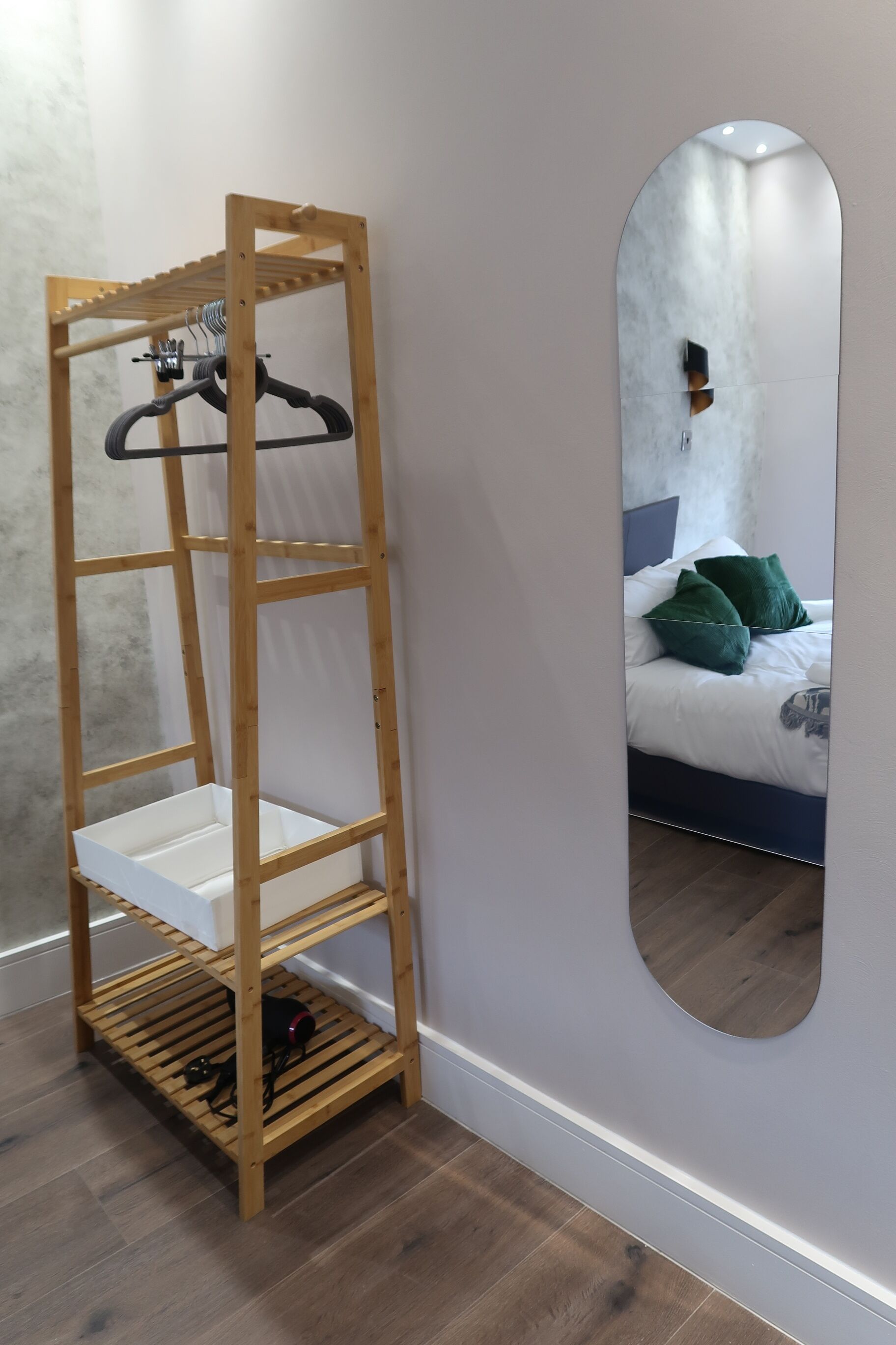 Une étagère en bois avec un miroir et un lit agrémenté d’oreillers verts.
