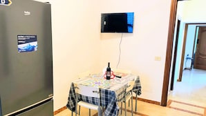 Una cocina compacta con refrigerador, una mesa de comedor con sillas y un televisor de pantalla plana montado.