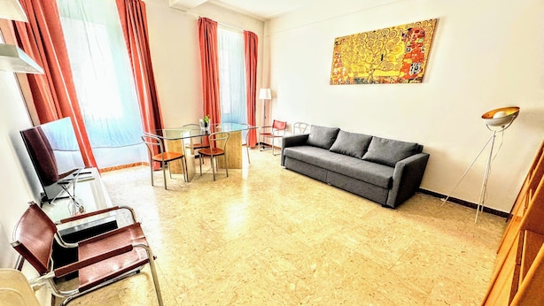 Una sala de estar moderna con un sofá gris, una mesa de centro de vidrio y un comedor con una pequeña mesa y sillas.