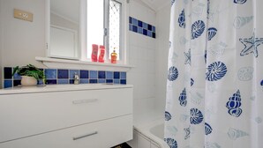 A bathroom with a white sink, blue tiles, a mirror, and a shower curtain with a shell pattern.