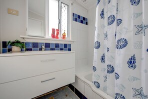 A bathroom with a white sink, blue tiles, a mirror, and a shower curtain with a shell pattern.