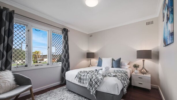 A bedroom with a bed, two bedside tables, a chair, a window with curtains, and a painting on the wall.