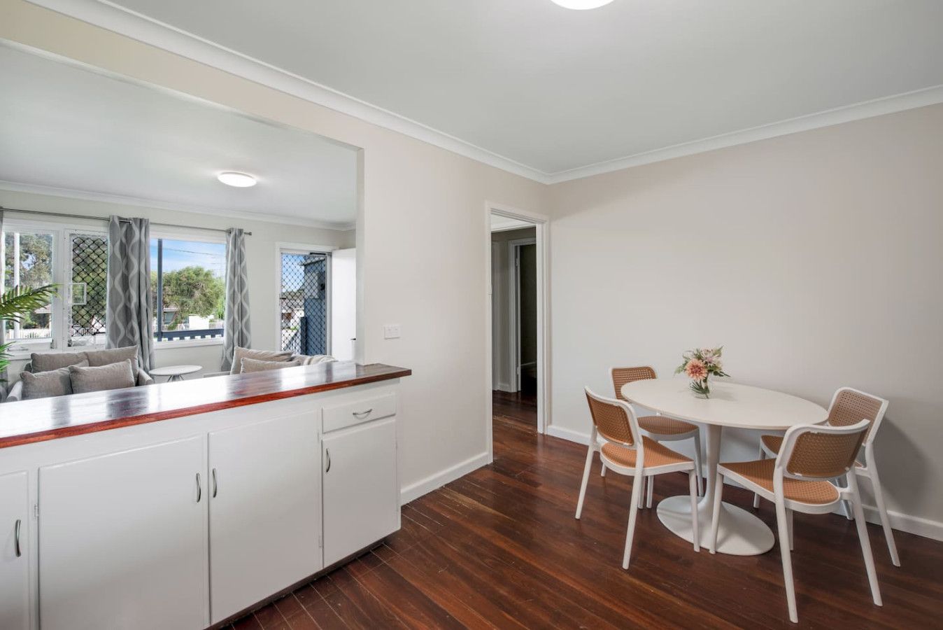 A modern kitchen with white cabinets, a wooden countertop, and a dining area with a white table and wicker chairs.