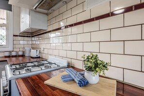 A modern kitchen with a gas stove, white cabinets, and a potted plant on the counter. - Older Cottage Style 3BR in Rangeway (Rangeway)