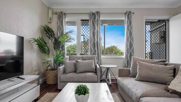 A modern living room with a sofa set, a coffee table, a TV, and a potted plant.