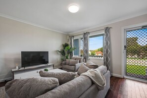 A modern living room with a flat-screen TV, grey sofa, and a sliding glass door leading to a balcony.