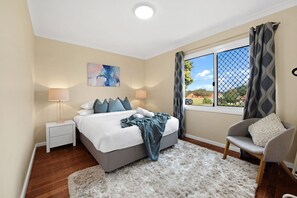 A bedroom with a bed, bedside tables, a chair, a window with curtains, and a painting on the wall.