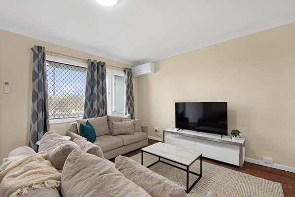 A living room with a beige sofa, a coffee table, and a TV on a white stand.