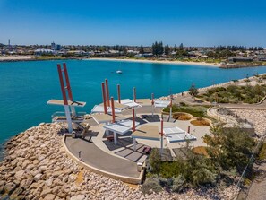 A coastal area with a rocky shoreline, a paved walkway, and several sun loungers with umbrellas.