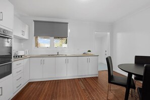 A modern kitchen with white cabinets, a black stove, and a dining area with a black table and chairs.