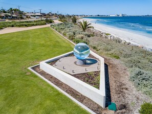 A landscaped area with a modern glass sculpture, a well-maintained lawn, and a beach in the background. - Rangeway Rescue - Older 3BR Home (Rangeway)