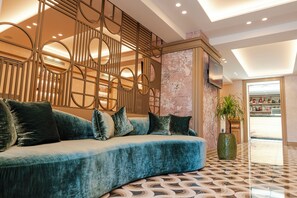 Eine moderne Hotellobby mit einer gebogenen, blauen Couch, dekorativen Wandverkleidungen, einer großen Vase und einem Fliesenboden.
