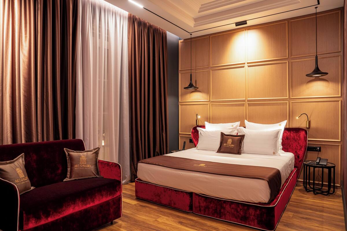Une chambre d’hôtel avec un grand lit, un canapé rouge et un mur recouvert de panneaux en bois.