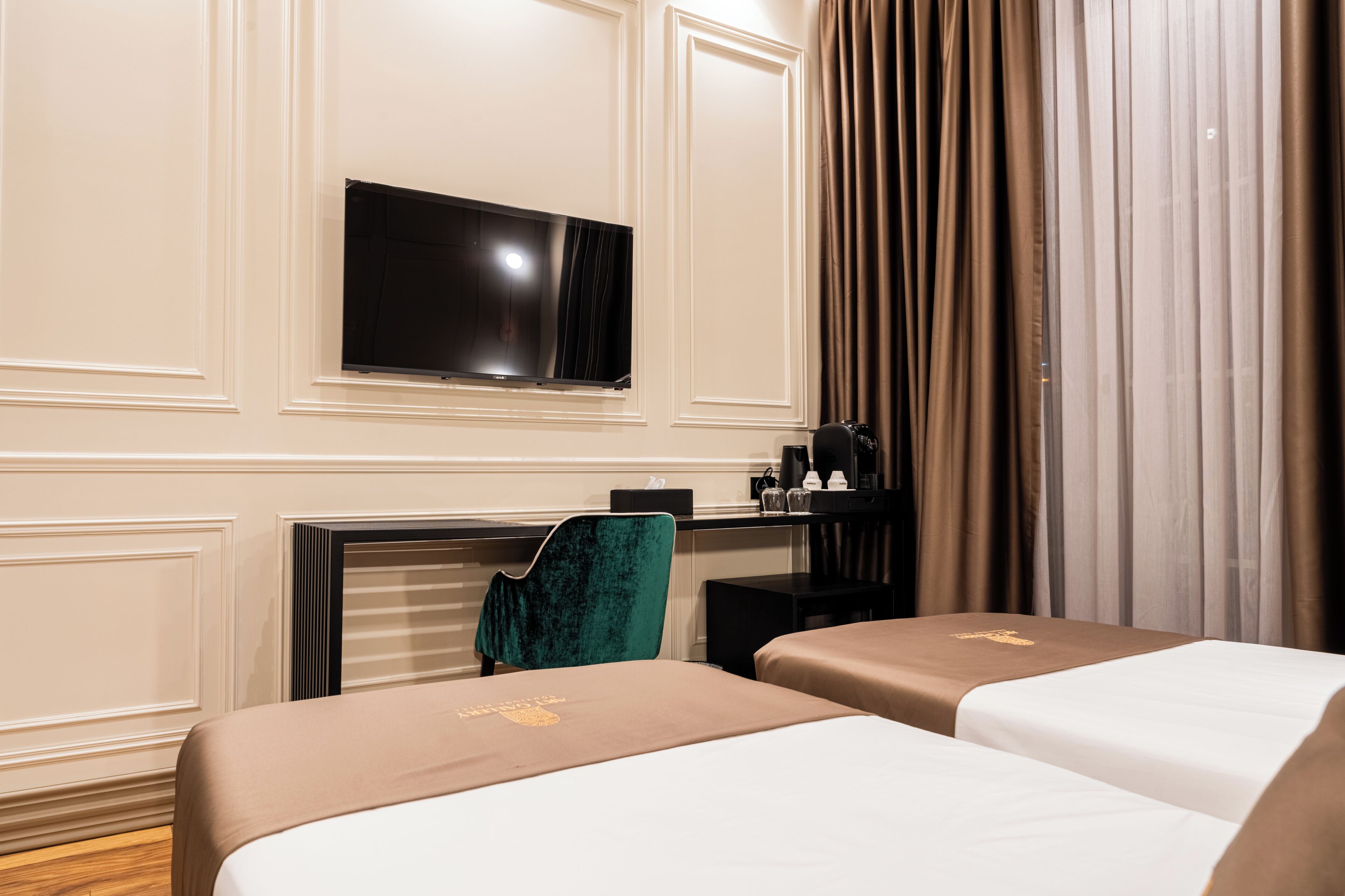 A hotel room with two beds, a TV, a desk, a chair, and a window with curtains.