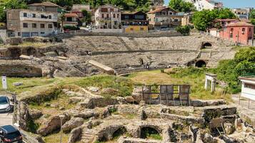 Alte Ruinen mit Steinbauten, einem teilweise erhaltenen Amphitheater und modernen Gebäuden im Hintergrund.