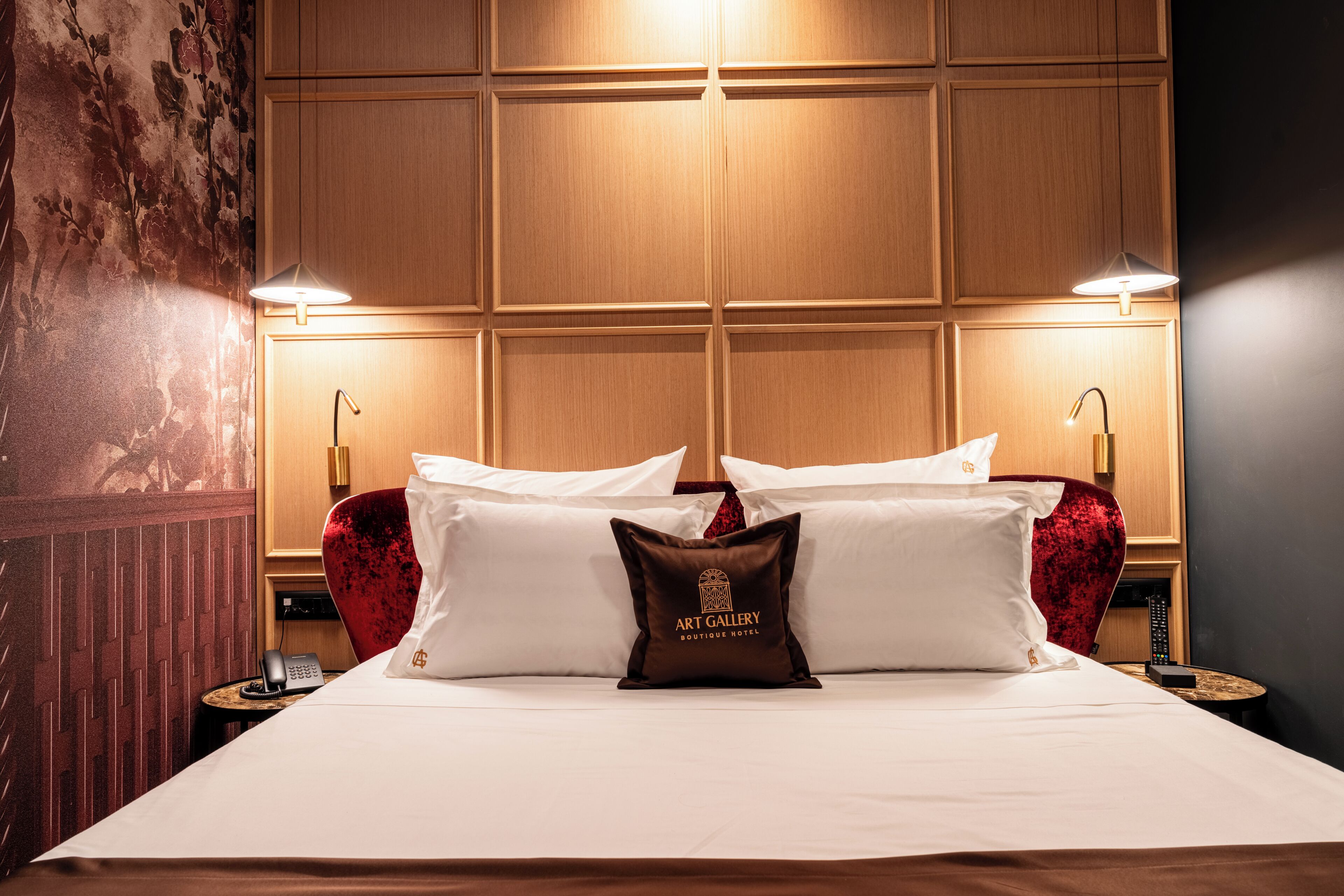 A hotel room with a large bed, two bedside lamps, a telephone, and a decorative pillow with 'Art Gallery Boutique Hotel' text.