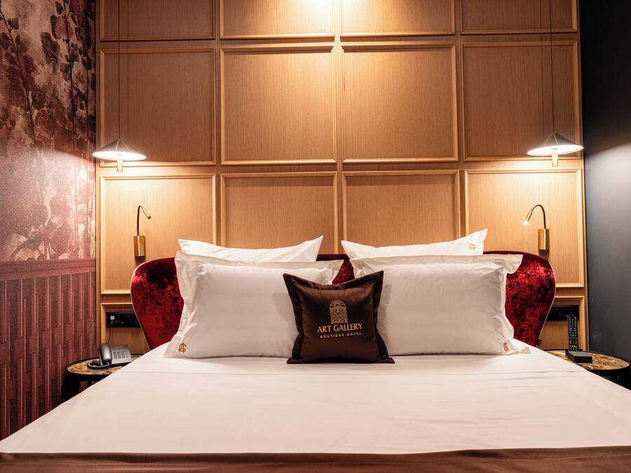 A hotel room with a large bed, two bedside lamps, a telephone, and a decorative pillow with 'Art Gallery Boutique Hotel' text.
