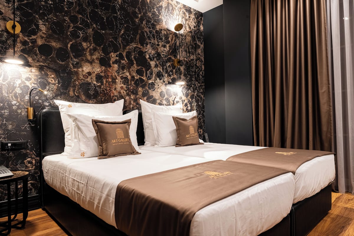Un lit double avec une literie blanche et marron, un mur à motifs de marbre et un luminaire moderne.